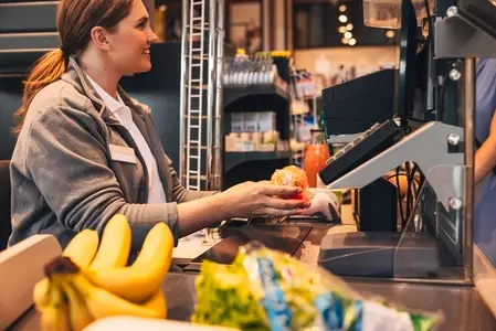 Side view of a female smiling cashier using barcode scanner on a pack on spaghetti focus on her hands Side view of a female smiling cashier using barcode scanner on a pack on spaghetti focus on her hands
