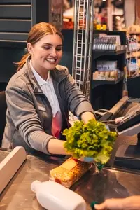 Cheerful woman cashier holding a salad while sitting at counter in grocery store