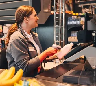 Smiling cashier using a barcode scanner on a bottle of milk in a grocery store