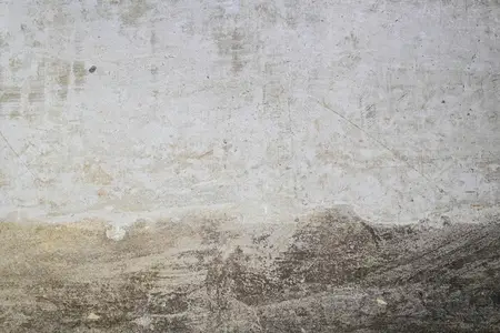 A close up photo of a textured concrete wall with visible stains  scratches  and weathered marks  The rough surface shows natural patterns and grunge details