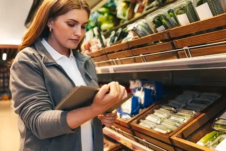 Young woman working in a grocery store holding a digital tablet