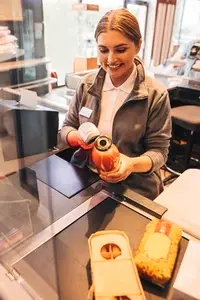 Smiling female cashier holding a bottle of juice and using a barcode scanner