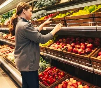 Grocery store employee adjusting shelves with fruits and vegetables