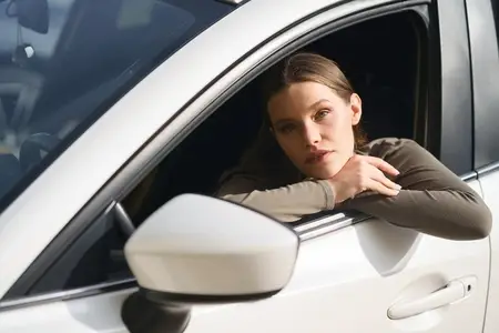 A Pensive Young Woman Sitting in a Car and Looking Out the Window Lost in Thought