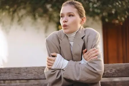 A Woman Sitting on a Park Bench Wearing a Cozy Sweater Feels Cold During Autumn Days A Woman Sitting on a Park Bench Wearing a Cozy Sweater Feels Cold During Autumn Days