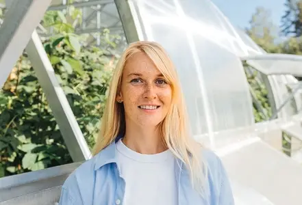 Smiling woman with blond hair and freckles standing at a greenhouse  Highly detailed portrait of a greenhouse worker standing outdoors