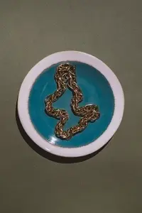 Vintage gold chain displayed in a ceramic plate with teal glaze on a green background  Minimalist still life composition with retro charm