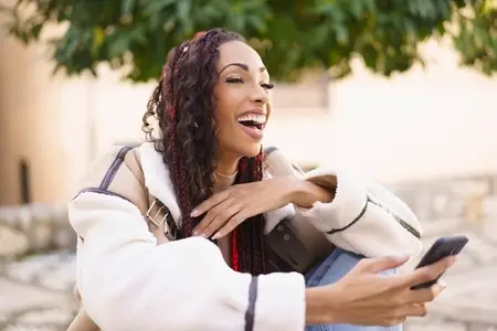 A Joyful Woman is Using Her Smartphone Outdoors while Experiencing Genuine Laughter and Relaxation