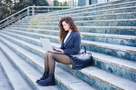 A young woman works intently on her laptop outdoors  displaying focus in a city setting