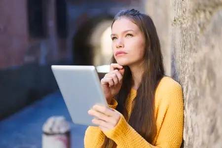 A Thoughtful Young Woman Engaged with Her Tablet While Sitting in an Urban Environment
