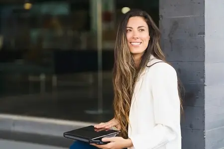 A Smiling Woman Enjoying a Coffee Break while Working on Her Laptop in an Urban Setting