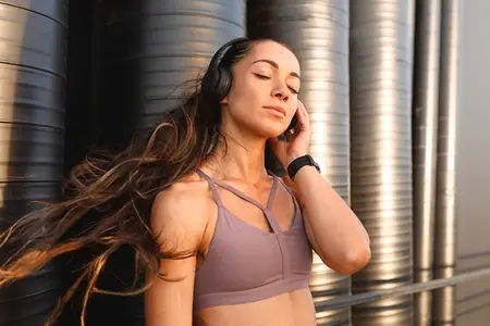 Young sportswoman with long hair enjoying music with closed eyes  Female listening to music on wireless headphones during a workout