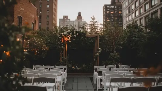 Urban outdoor wedding ceremony with white chairs  floral arch  city buildings  romantic evening