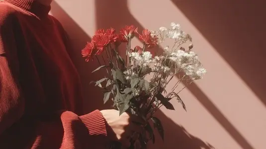 Woman in red sweater holding bouquet of red and white flowers in soft sunlight  minimal aesthetic