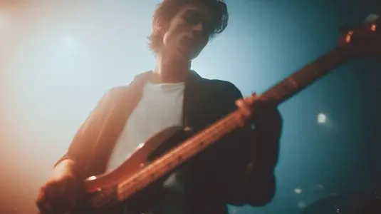 Young male musician playing electric bass guitar on stage with moody lighting  indie vibe