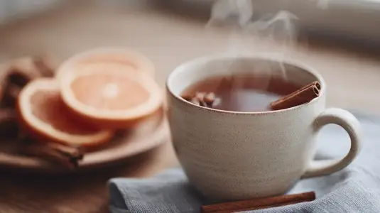 Steaming cup of herbal tea with cinnamon stick and orange slice on wooden table  cozy atmosphere