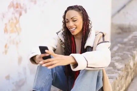 A young woman sits outdoors with her smartphone  enjoying the fresh air and vibrant atmosphere