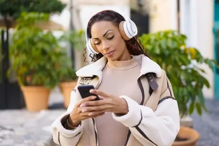 A Young Woman Joyfully Enjoying Her Favorite Music While Outdoors Using a Smartphone with Headphones