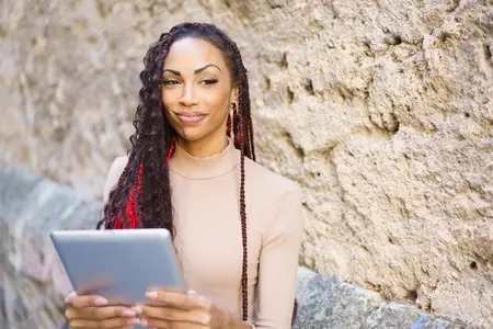 A Confident Woman Engaged in Using a Tablet While Seated Against a Stone Wall Background