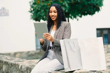 A Stylish Woman Engaging in Online Shopping Using Her Tablet While Surrounded by Shopping Bags