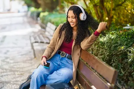 A young woman is happily enjoying some music while sitting in the park with headphones on