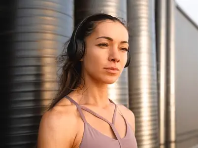 High detailed portrait of young female wearing wireless headphones standing outdoors at sunset