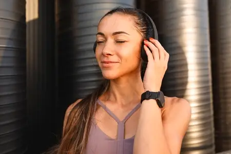 Satisfied young sportswoman with wireless headphones listening to music with closed eyes