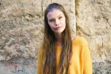 A Young Woman Dressed in a Bright Yellow Sweater Posing Elegantly Against a Stone Wall