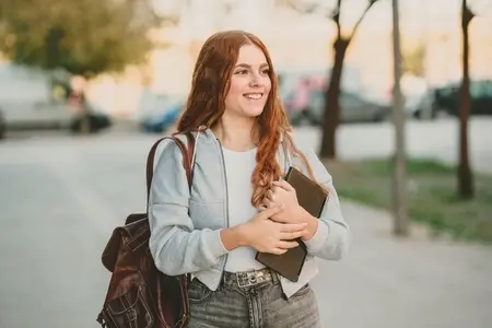 A Joyful Young Woman Walking through a Vibrant Urban Setting while Holding a Notebook