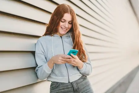 A young woman is texting on her smartphone while standing against a vibrant  modern background