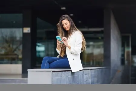 A young woman is using her smartphone outdoors while surrounded by a modern urban environment