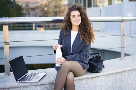 A Smiling Professional Woman Enjoying Her Laptop and a Refreshing Drink in an Urban Setting