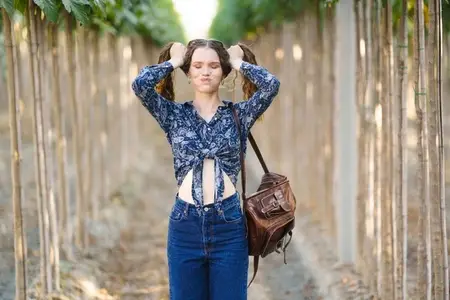 A young woman wearing a floral top paired with denim jeans is situated in a serene natural setting