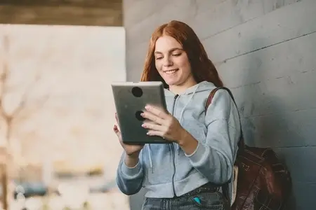 A joyful teenage girl is savoring engaging digital content on her tablet while outdoors