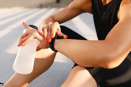 Close up of female hands holding a sports bottle and checking smartwatches during a workout