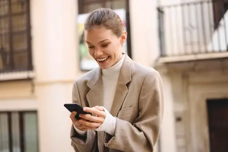 A Charming Smiling Woman Engaged in Texting on Her Smartphone While in an Urban Setting
