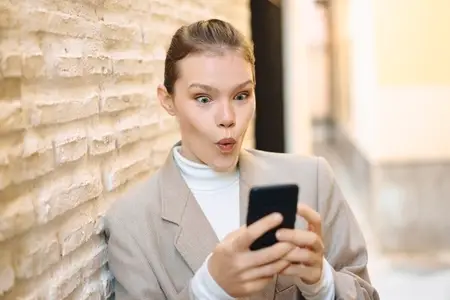A surprised woman is engaged with her smartphone while sitting in a modern and vibrant setting