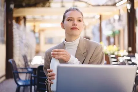A thoughtful young professional sits in a cafe with their laptop  immersed in work and reflection