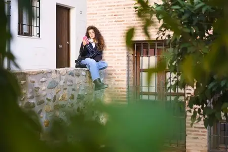 A Young Woman with Beautiful Curly Hair is Sitting on a Wall in an Urban Environment