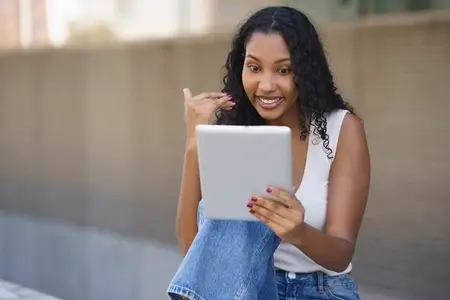 A Young Woman is Actively Engaged in a Video Call Outdoors Using Her Tablet Device