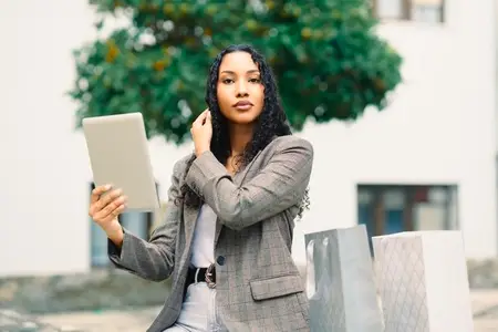 A Stylish Young Woman Engaging Enthusiastically with a Tablet Amidst Shopping Bags Around Her