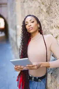 A Confident Woman Holding a Tablet in a Vibrant Urban Setting on a Beautiful Day
