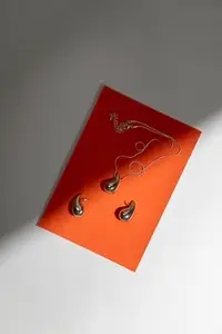 Elegant golden jewelry set with pendant and earrings on orange background in minimal modern composition with shadow and light