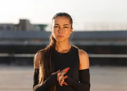 Young woman athlete wearing sportswear and arm sleeves standing outdoors and looking at camera at sunset