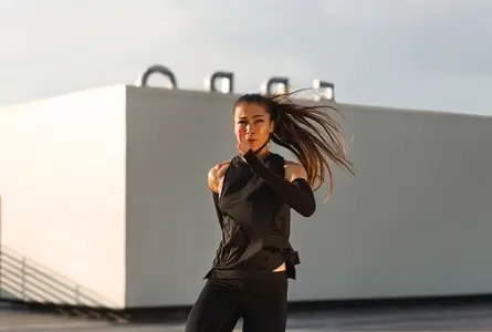 Young female in black fitness attire practicing an intense workout  Woman with long hair jumping and warming up on the roof at sunset