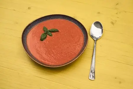 Still life of gazpacho garnished with basil in bowl next to spoon