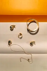 Elegant gold jewelry set with earrings  bracelet and necklace on beige and orange background in minimal modern style