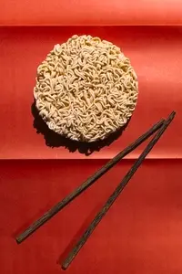 Round block of instant noodles with wooden chopsticks on red background  minimal food concept with strong contrast and shadow