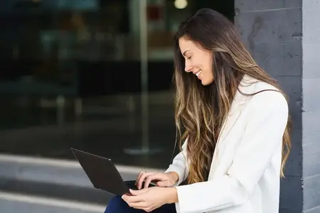 A Happy Smiling Woman Engaged with Her Laptop in a Modern Outdoor Setting  Embracing Productivity