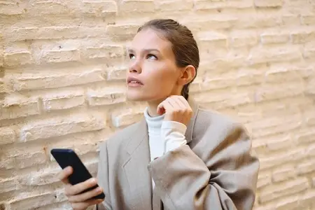 A Thoughtful Young Woman Engaged Indirectly with Her Smartphone Against a Textured Wall